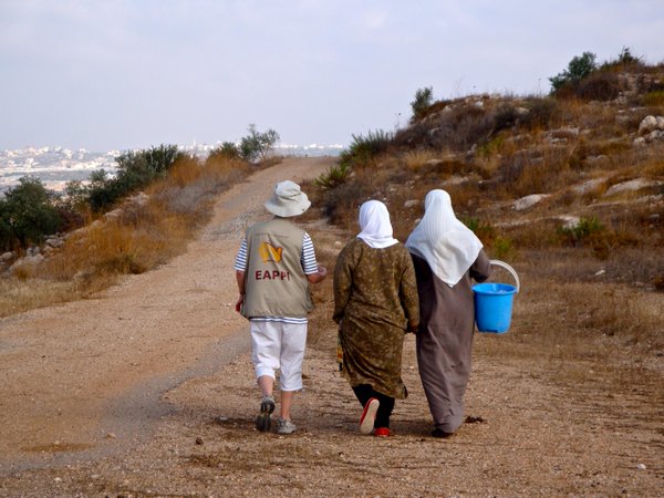 Three women, one of whom is an eccumenical accompanier, walking down a road in the West Bank