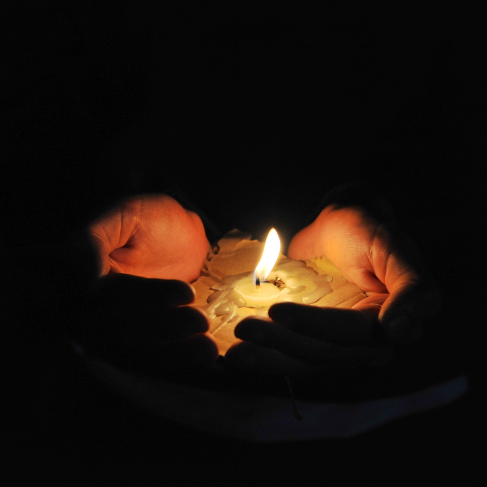 A candle held in two hands that are filled with melted wax