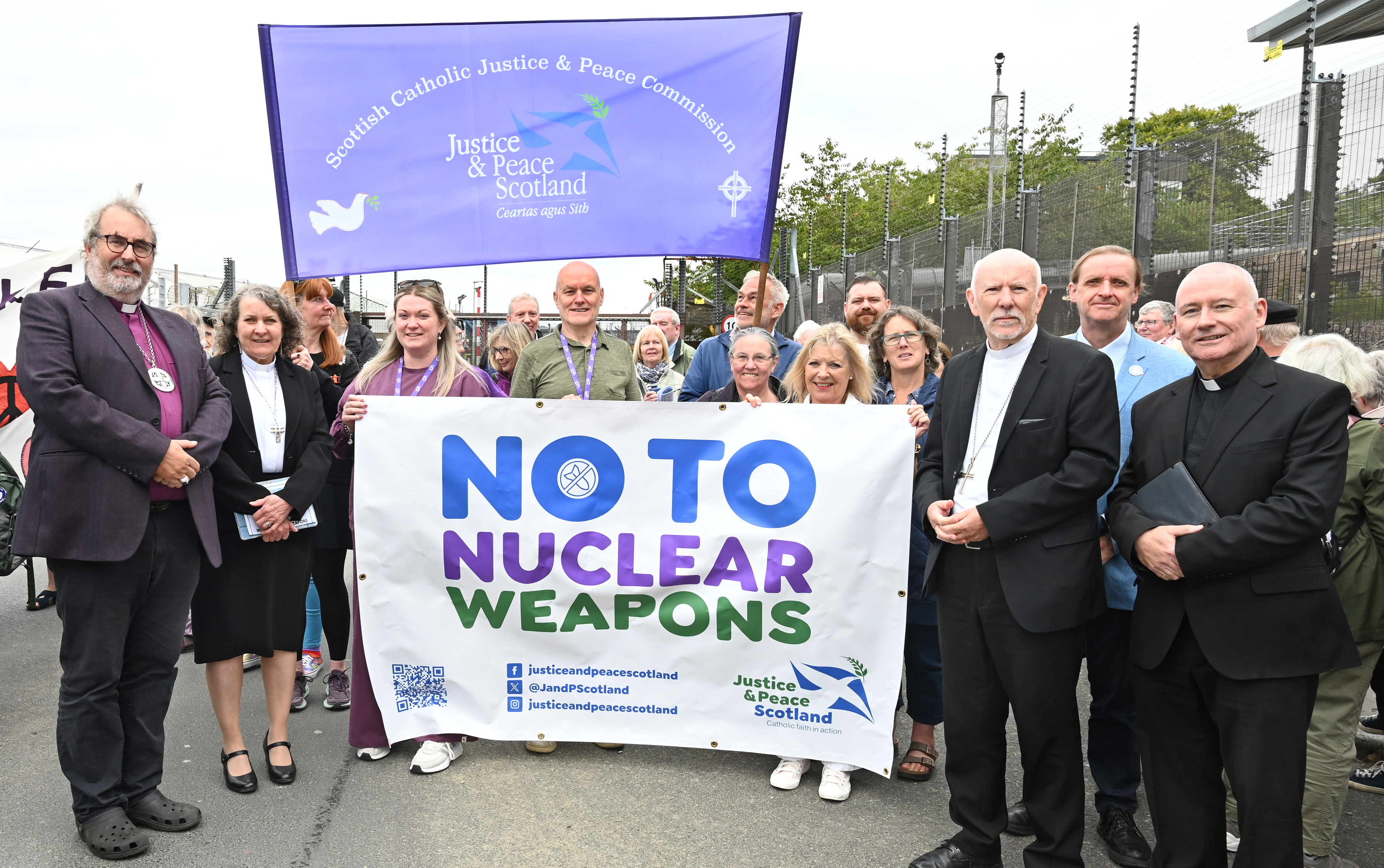 A photograph of Christian leaders at Faslane with banners reading No to Nuclear Weapons and Scottish Catholic Justice and Peace Commission