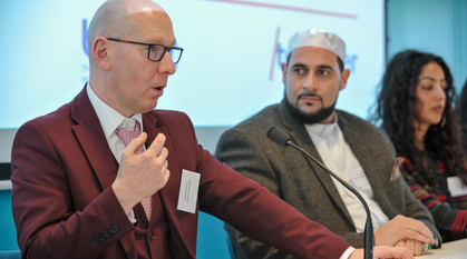 A photograph of Patrick Hurley MP speaking in a panel. He is gesturing and the person next to him is listening intently.