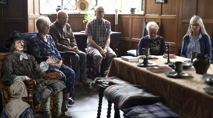 Illustrations of George Fox and Margaret Fell sitting in a photograph among a modern meeting for worship at Swarthmoor Hall (their home)
